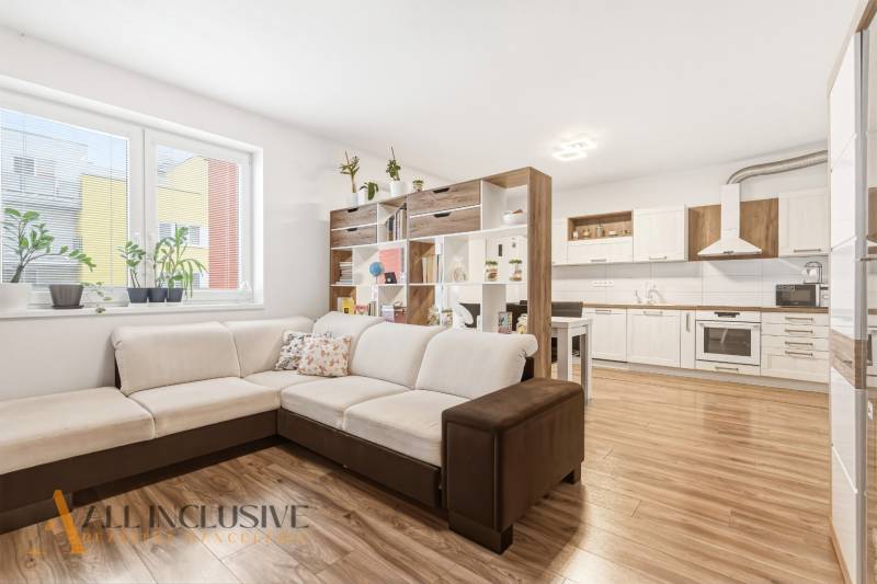 Nappali egy kétszobás lakásban nagy kanapéval és konyhával, fa dekorációjú padlóval.