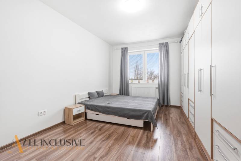 Hálószoba egy kétszobás lakásban, fa mintázatú padlóval, fehér szekrényekkel és szürke részletekkel.