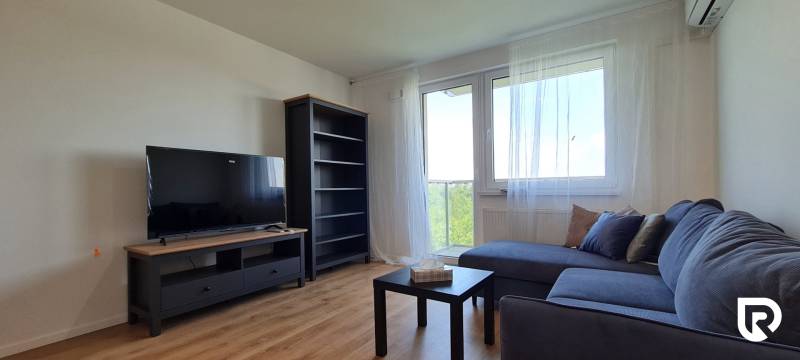 Nappali egy kétszobás lakásban kanapéval, televízióval és fa dekorációjú padlóval.