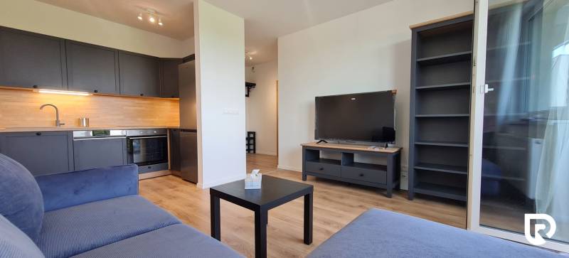 Kétszobás lakás konyhabútorral, kék kanapéval, televízióval és fa mintázatú padlóval.