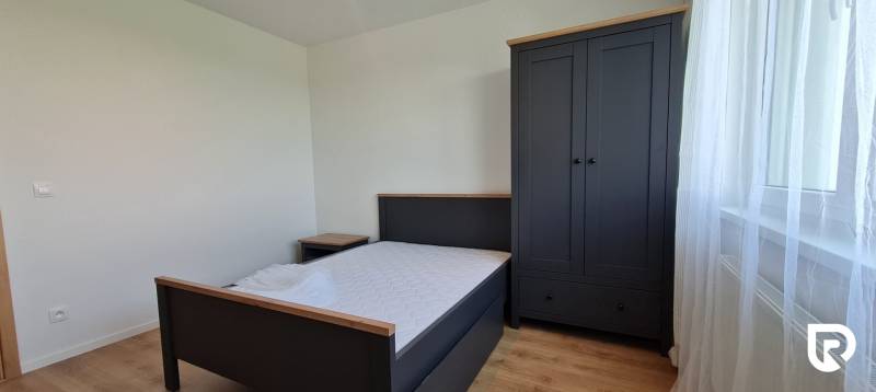 A kétszobás lakás hálószobája tartalmaz egy ágyat, éjjeliszekrényt, ruhásszekrényt és fa dekorációjú padlót.