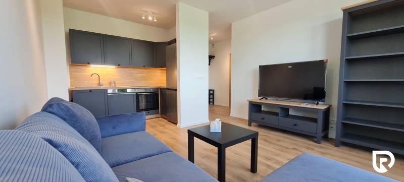 Nappali konyhasarokkal, szürke kanapéval és fa dekorációjú padlóval egy kétszobás lakásban.