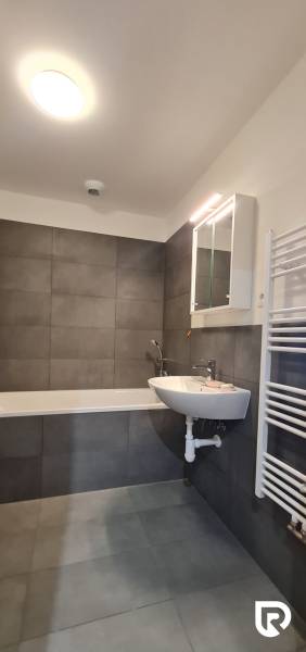 Fürdőszoba egy kétszobás lakásban káddal, mosdóval és tükrös szekrénnyel.