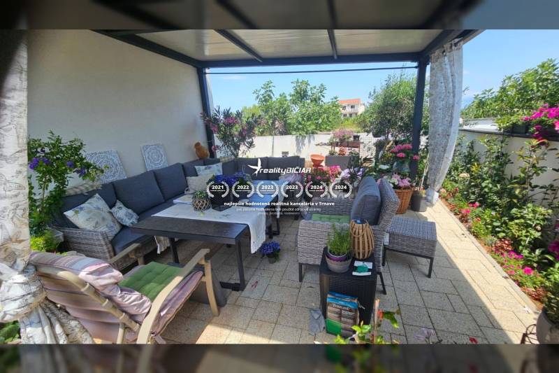 Pihenés a teraszon a nyaraló apartmanban kényelmes ülőalkalmatossággal, virágdíszítéssel és asztallal.