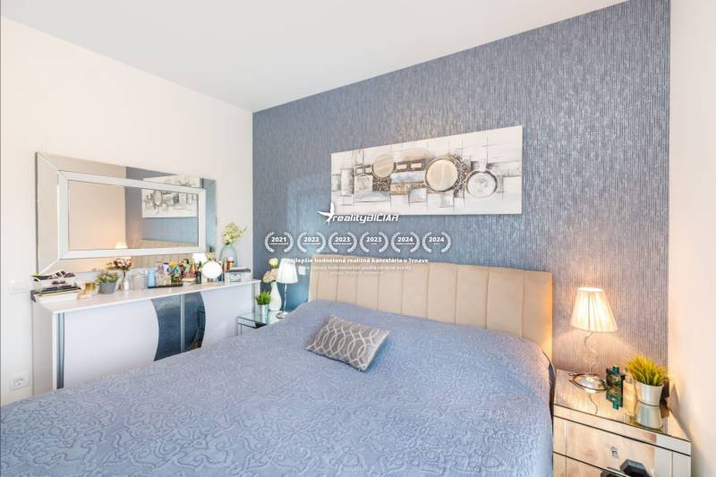 Hálószoba a nyaraló apartmanban kék ágytakaróval, dekorációkkal és tükörrel az asztal felett.