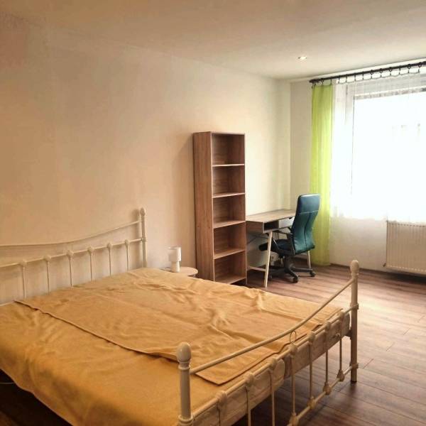 Hálószoba ággyal, asztallal, polccal és fa dekoros padlóval egy kétszobás lakásban.