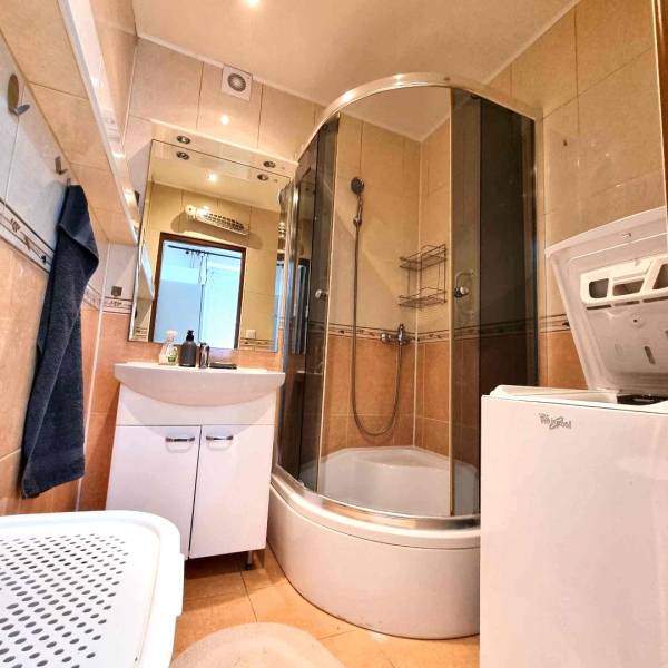 Fürdőszoba egy kétszobás lakásban üveg zuhanykabinnal és mosógéppel.