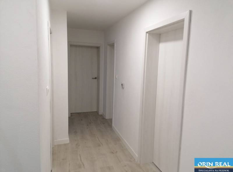 Folyosó egy családi házban fehér falakkal és fa mintázatú padlóval.