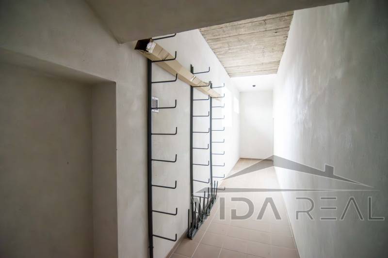 Keskeny belső tér egy raktárban, falon fém akasztókkal.