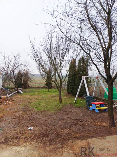 Vizsolyi családi ház kertje fákkal és gyerekhintával a gyepen.