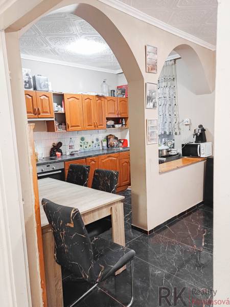 Családi ház konyhája íves bejárattal, fa szekrényekkel és fekete padlóval.