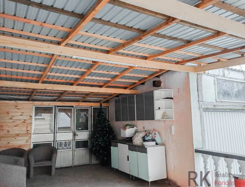 Családi ház: Fém tetős kocsibeálló, rattan székek, műnövények, tárolóhelyek.