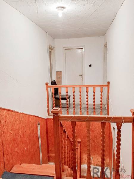 Lépcsőház fa korláttal családi házban, fehér falak, világítás izzóval.