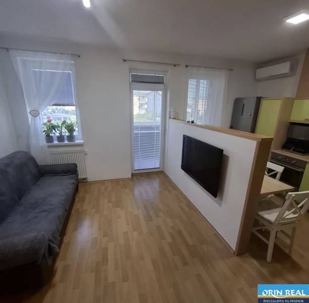 Nappali egy kétszobás lakásban kanapéval, televízióval, fa dekoros padlóval és erkéllyel.