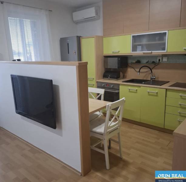 Konyha egy kétszobás lakásban zöld szekrényekkel, televízióval és egy asztallal két székkel.