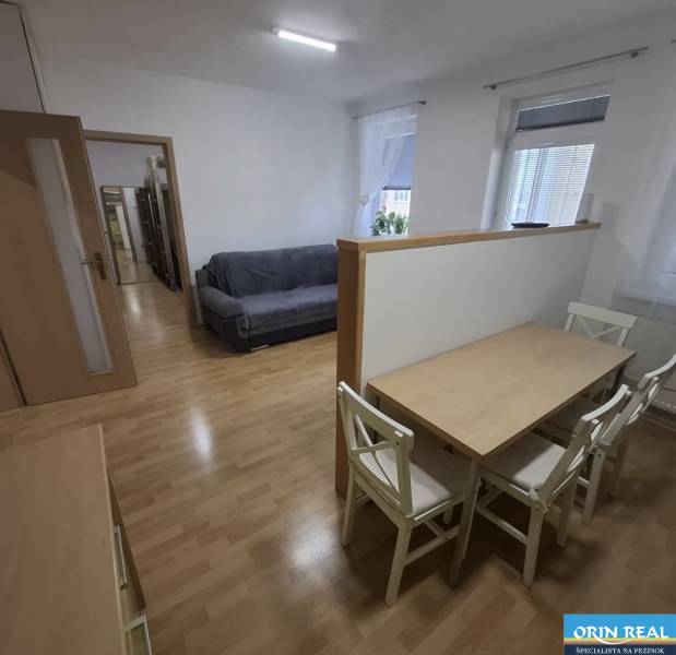 Nappali kanapéval, étkezőasztallal és fa dekorációjú padlóval egy kétszobás lakásban.