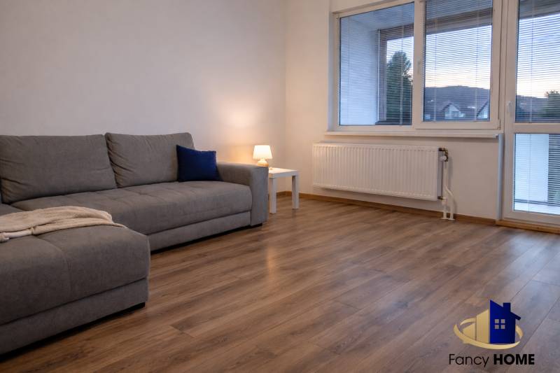 Nappali egy háromszobás lakásban kanapéval és fa dekorációjú padlóval.