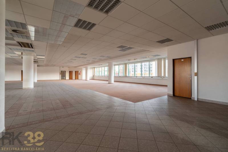 Tágas irodák ablakokkal, fa mintázatú padlóval és oszlopokkal.