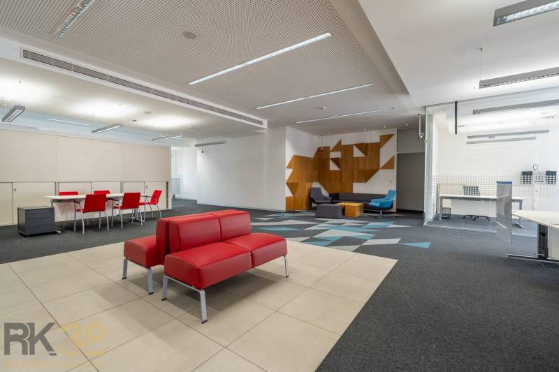 Irodák piros kanapékkal, konferenciaasztallal, mintás szőnyeggel és fa dekorációkkal.