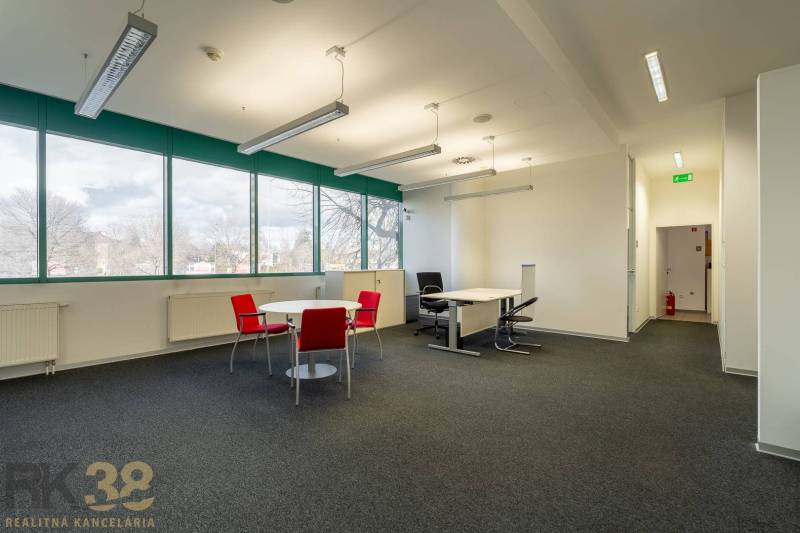 Irodák fekete szőnyeggel, piros székekkel és nagy ablakokkal a földszinten.