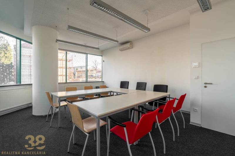 Iroda belső tér hosszú asztallal, színes székekkel és nagy ablakokkal.