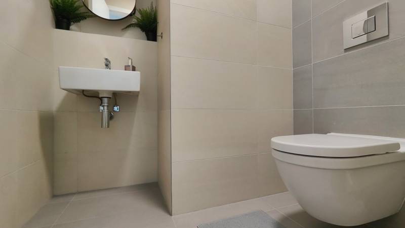 Két szobás lakás fürdőszobája függesztett WC-vel, mosdóval és fehér csempékkel.