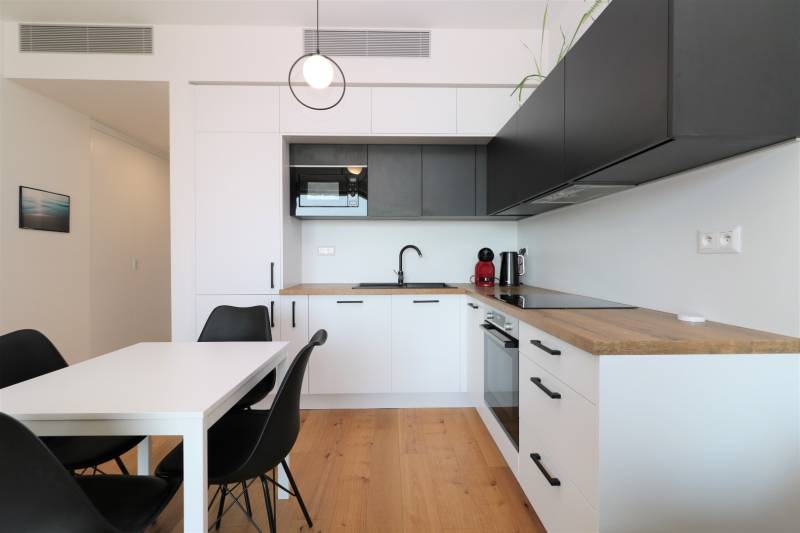 Konyha egy kétszobás lakásban, fa dekoros padlóval és fekete szekrényekkel.