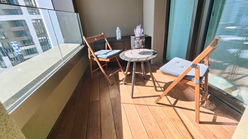 Erkély fa dekorációjú padlóval, ülőhely és díszasztal egy kétszobás lakásban.