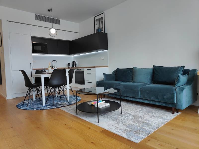 Nappali konyhasarokkal, türkiz kanapéval, fa dekorációval és étkezőasztallal.