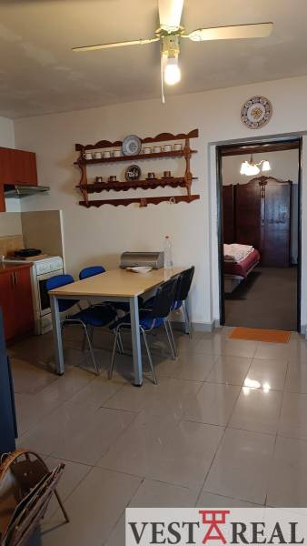 Családi ház étkezőasztallal és székekkel, konyhai rész és nyitott ajtó a hálószobába.