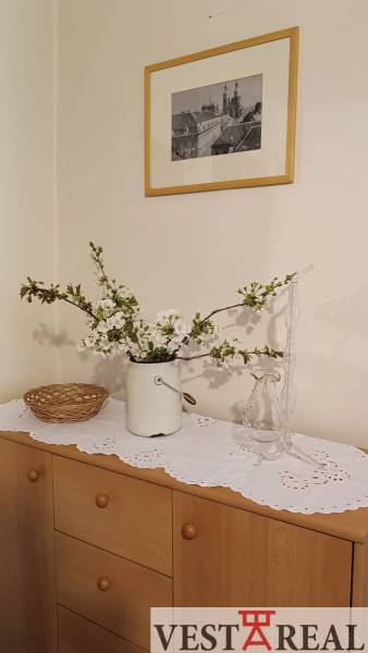 Családi ház virágokkal a komódon, díszes terítővel és képpel a falon.