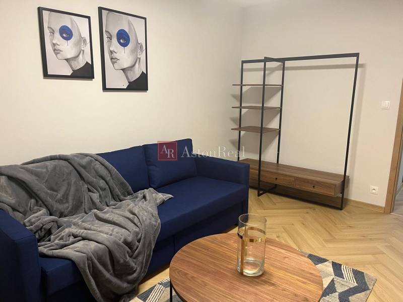 Nappali kék kanapéval, modern képekkel és polcrendszerrel egy háromszobás lakásban.