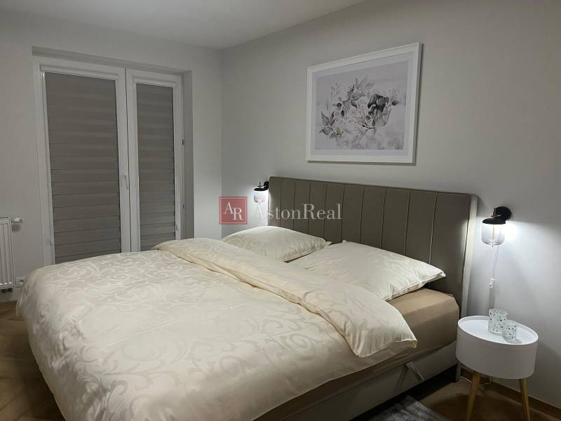 Hálószoba egy háromszobás lakásban világos ággyal és finom fali dekorációval.