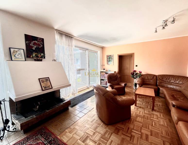 Családi ház kandallóval, kanapékkal, képekkel a falon és fa dekorációjú padlóval.