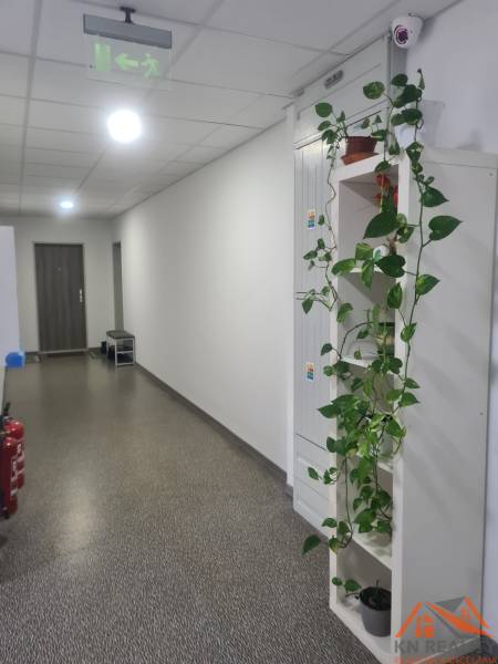 Két szobás lakás folyosója csempével, növényzettel és menekülési jelzéssel a mennyezeten.