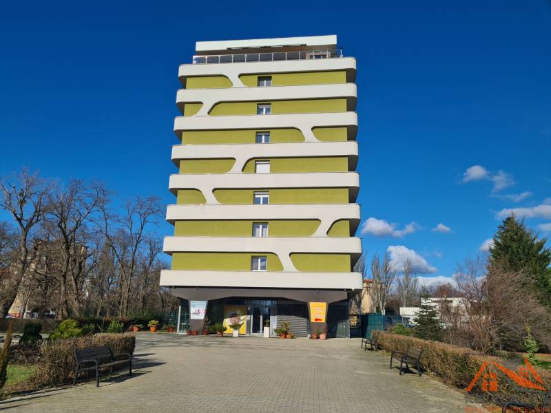 Többszintes lakóépület Komáromban, modern dizájnnal, zölddel és padokkal körülvéve.