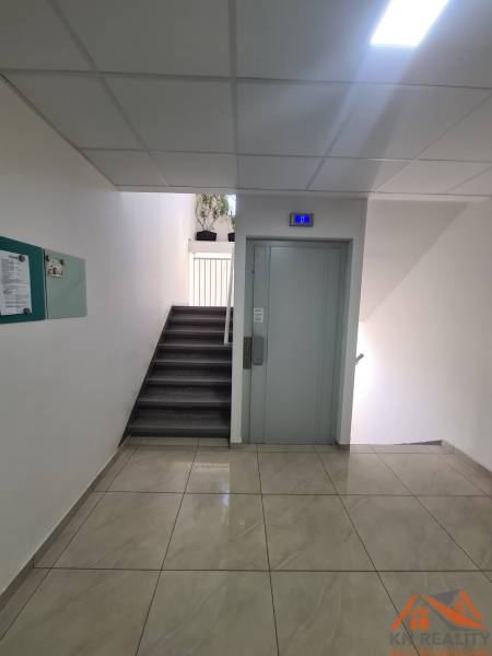 Lépcsőház lifttel, burkolattal és növényekkel egy kétszobás lakásban.