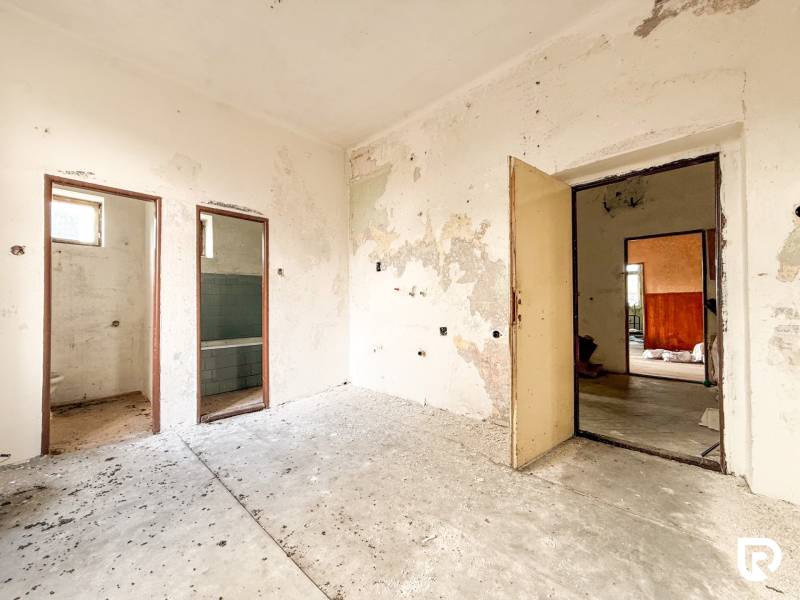 Egy családi házban van egy régi szoba, kopott falakkal és fedetlen helyekkel.