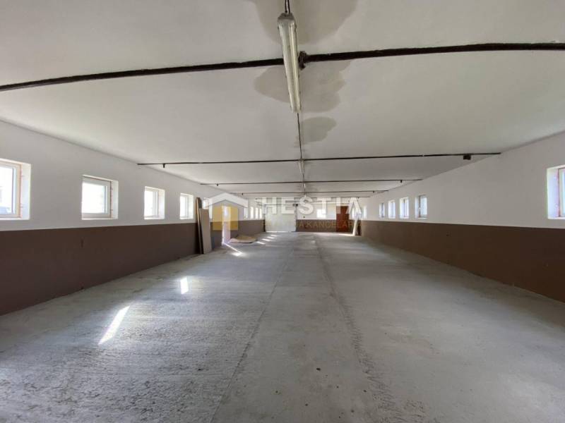 Tágas raktár és csarnok belső tér ablakokkal mindkét oldalon, betonpadlóval.