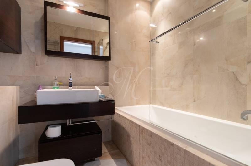 Fürdőszoba káddal és sötét bútorokkal egy kétszobás lakásban, világos csempékkel.