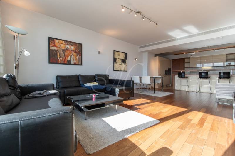 Nappali egy kétszobás lakásban fa dekor padlóval és fekete bőr kanapéval.