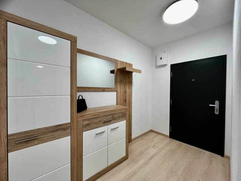 Folyosó fa dekorpadlóval egy 2 szobás lakásban, modern bútorokkal és sötét ajtókkal.