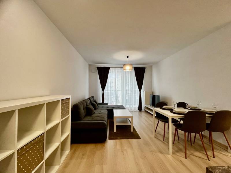 Nappali egy kétszobás lakásban kanapéval és étkezőasztallal, fa mintázatú padlóval.