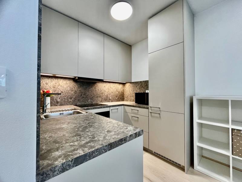 Konyha egy kétszobás lakásban kő munkalappal és fehér szekrényekkel.