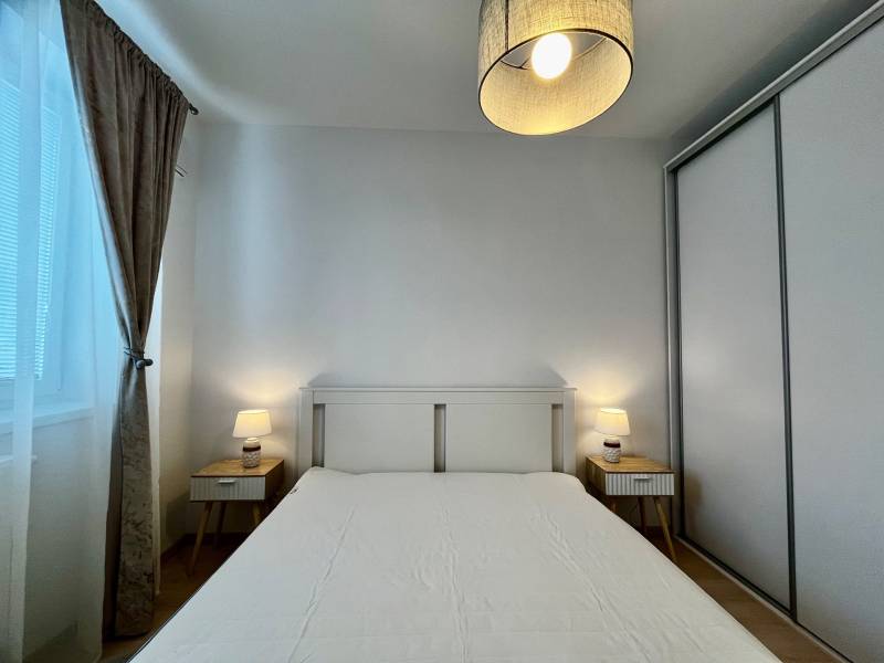 Hálószoba egy kétszobás lakásban fehér ággyal, éjjeliszekrényekkel és lámpákkal.