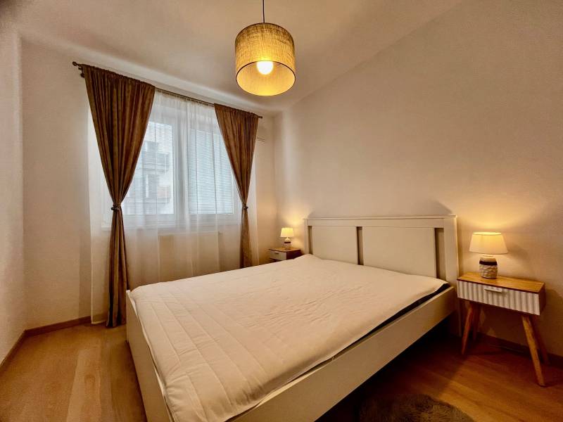 Hálószoba nagy ággyal, függönyökkel és fa dekorációjú padlóval egy kétszobás lakásban.