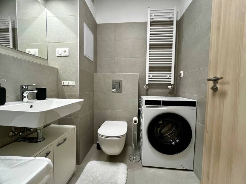 Fürdőszoba egy kétszobás lakásban mosdóval, mosógéppel és WC-vel, modern csempékkel.