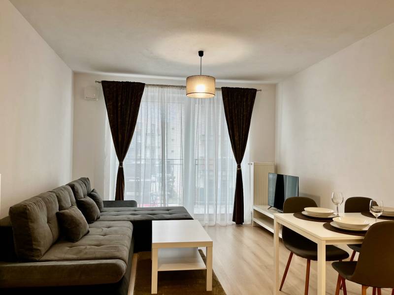 Nappali egy kétszobás lakásban kanapéval, étkezőasztallal és fa mintázatú padlóval.