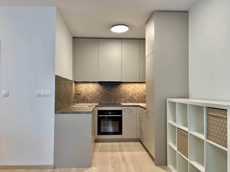 Konyha egy kétszobás lakásban fa hatású padlóval és tároló polcokkal.