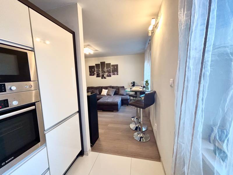 Konyhasarok készülékekkel, bárpulttal és kilátással a nappalira egy kétszobás lakásban.